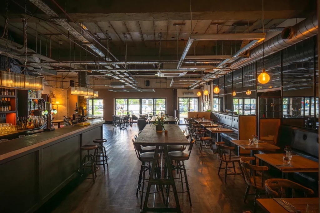 Pub dining area at The Hill with a long communal table, booth seating and large street facing windows.