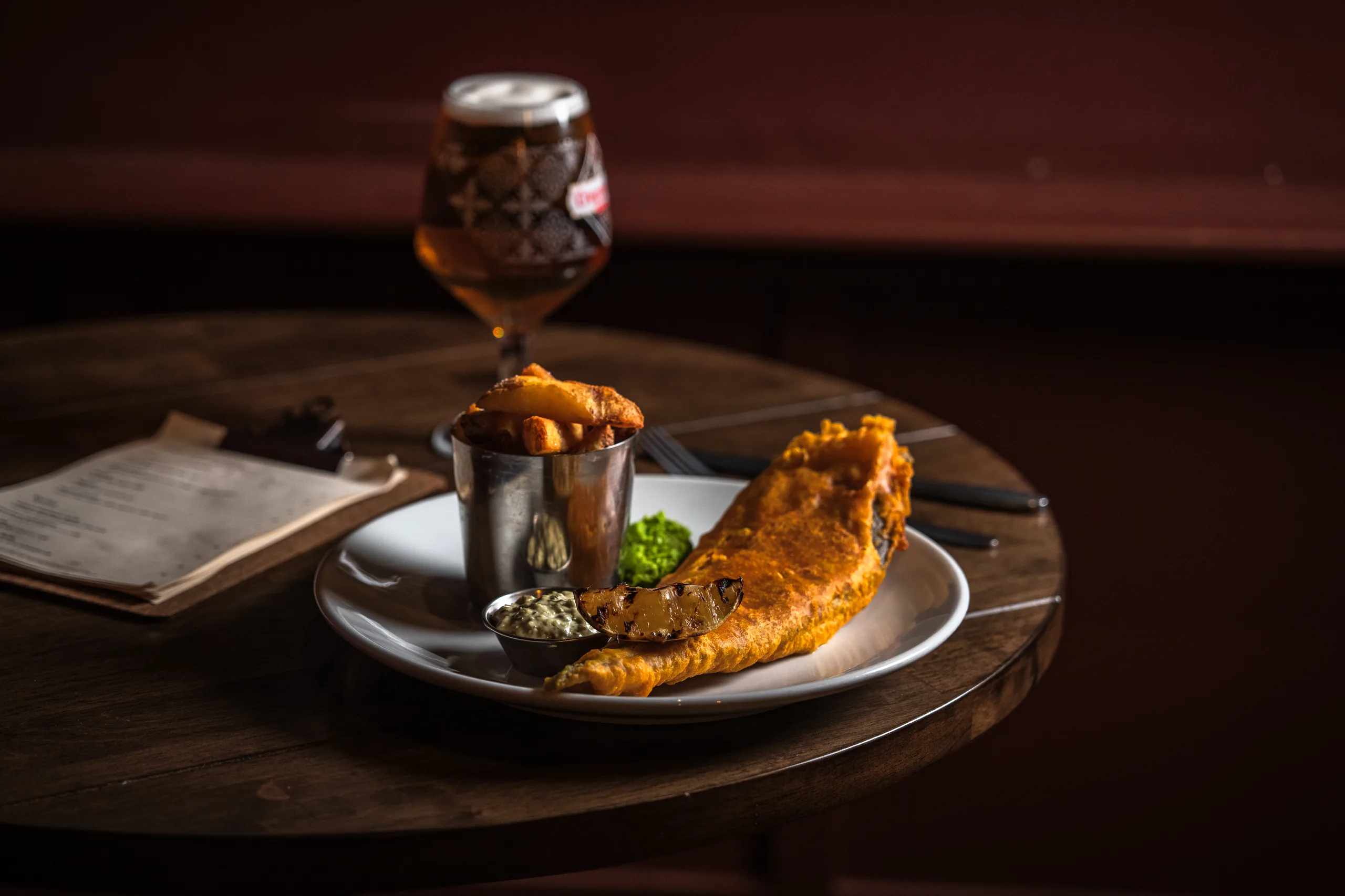 Battered fish and chips with mushy peas and a pot of tartare sauce, served with a pint of ale.