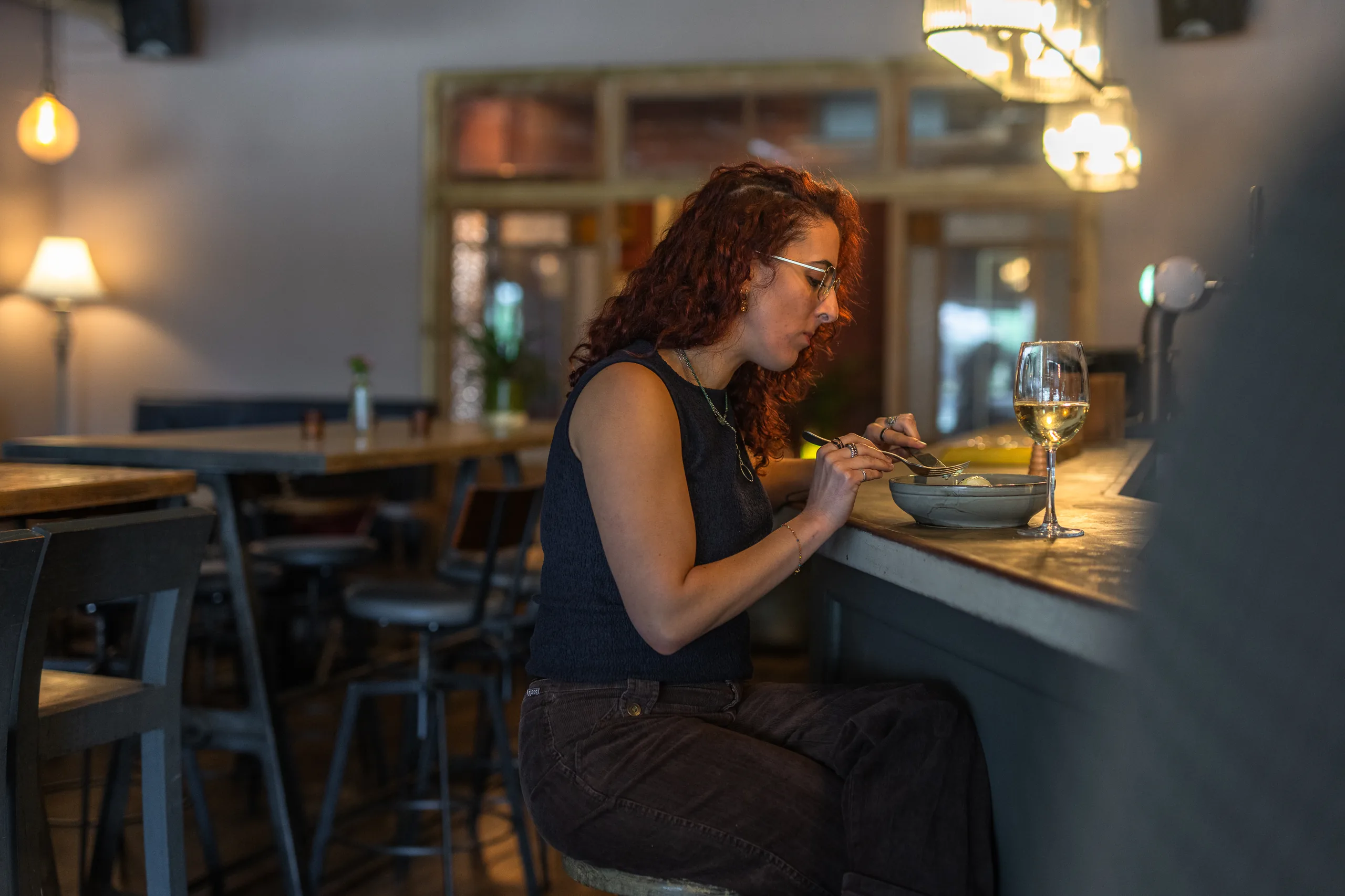 A guest sitting at the bar counter eating a bowl of food with a glass of white wine.