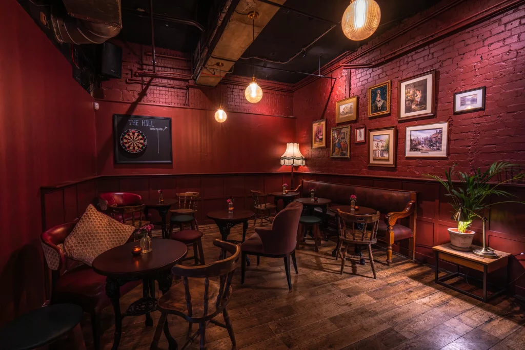 Intimate dining room with deep red brick walls, framed pictures, a dartboard and traditional pub seating.