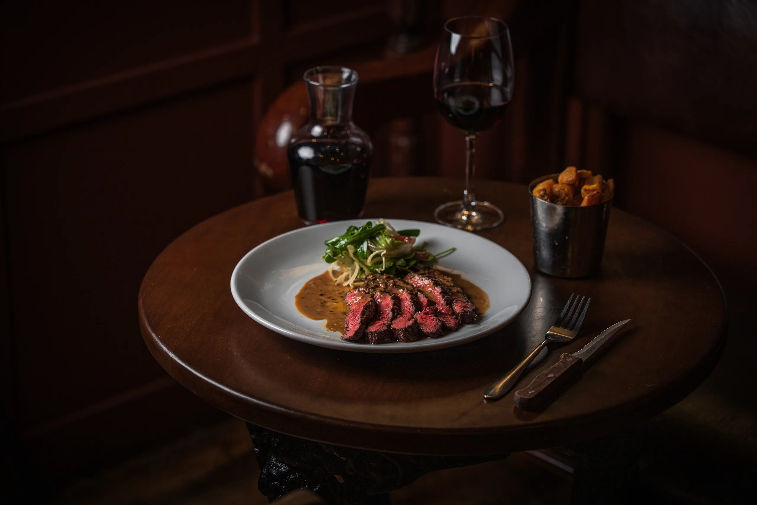 Sliced bavette steak with peppercorn sauce, a watercress salad and a cup of triple cooked chips, served with red wine.