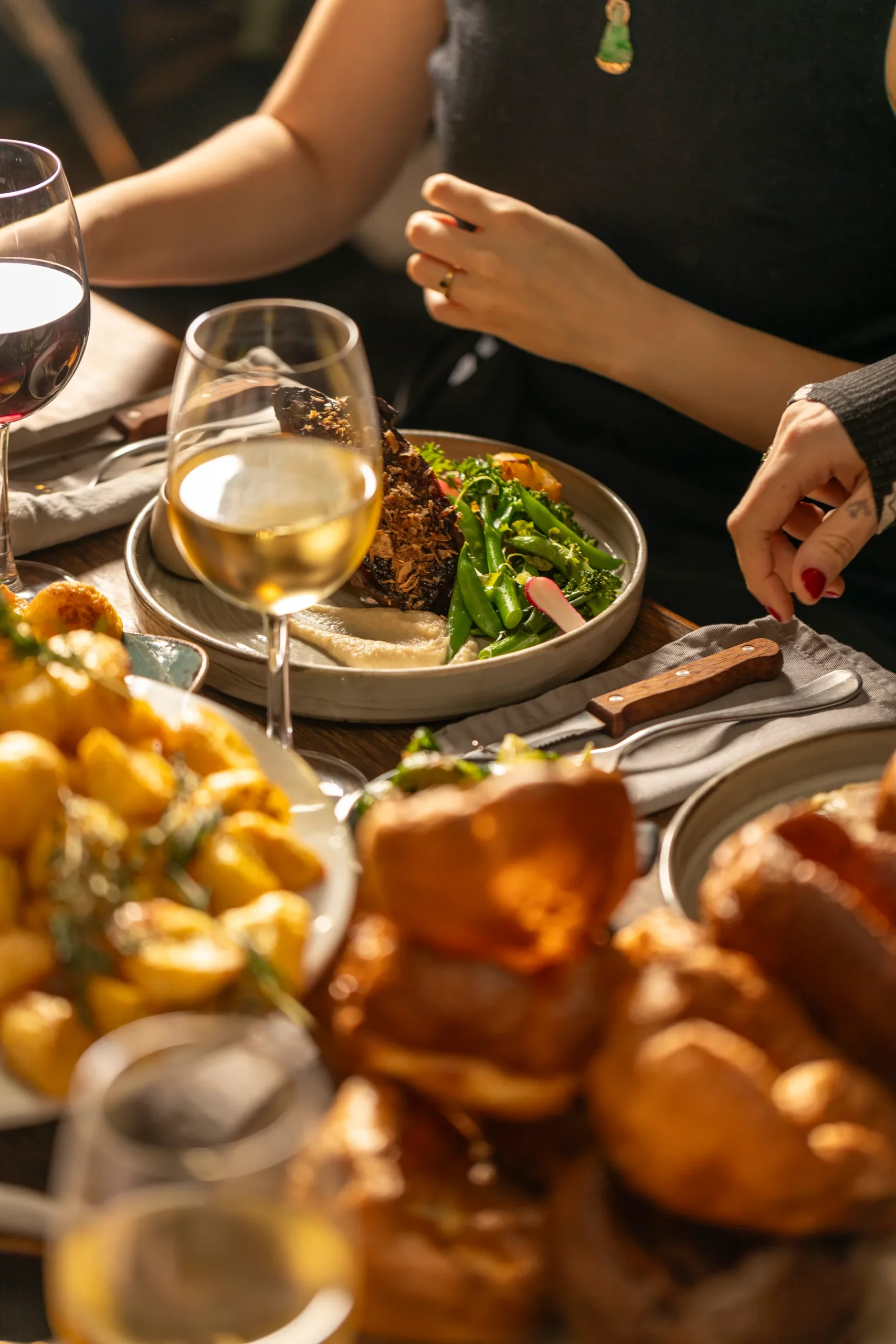 A plate of dark caramelised roast beef topped with crispy shallots and celeriac puree with seasonal greens, on a Sunday roast table at The Hill with roast potatoes, Yorkshire puddings and wine.