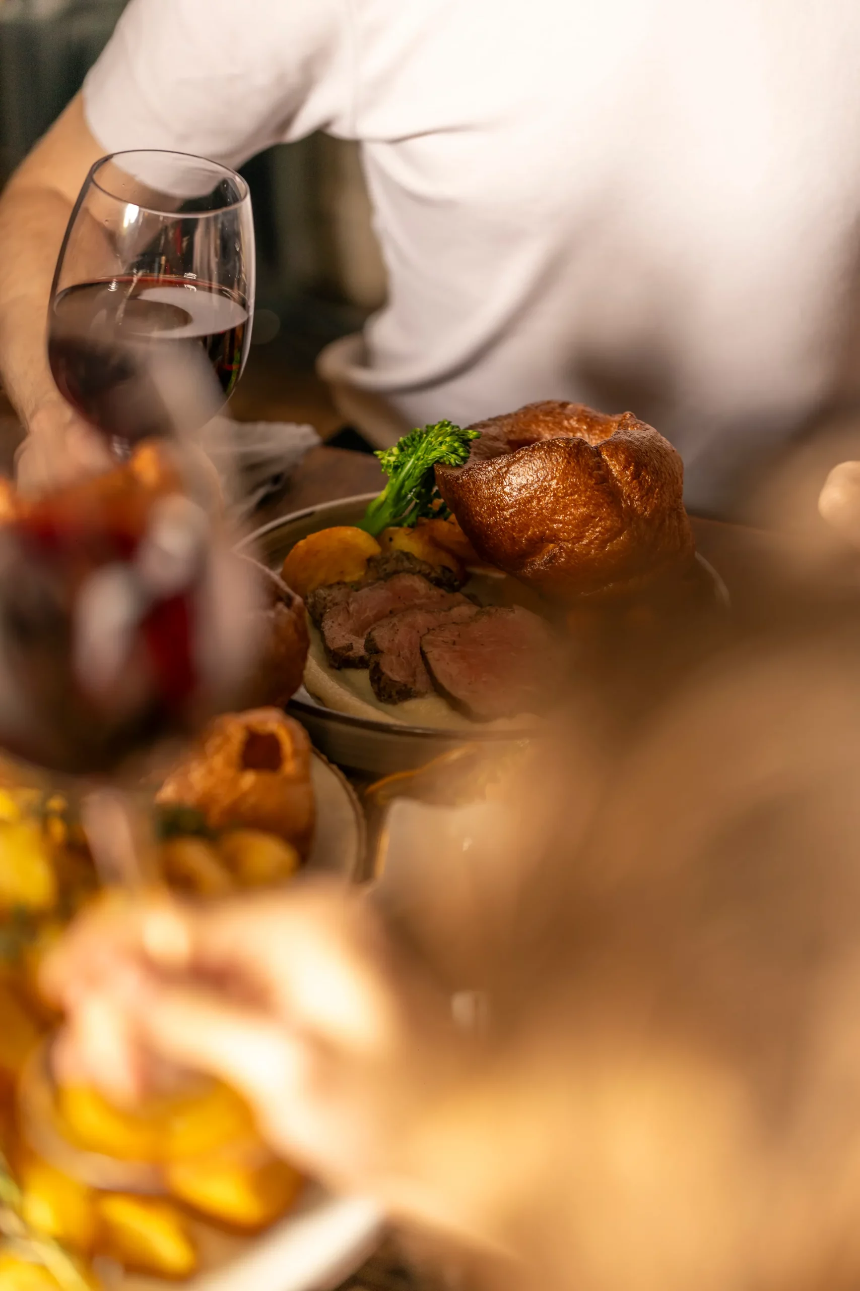 Slices of pink peppercorn-crusted roast sirloin of beef served with a tall golden Yorkshire pudding, roast potatoes and tenderstem broccoli, with a glass of red wine alongside.